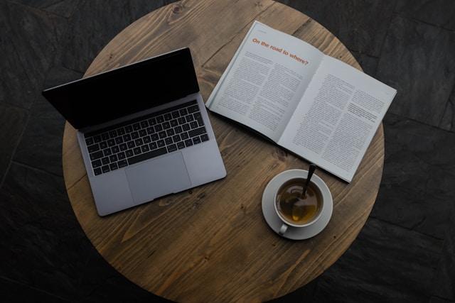 photo of a computer on the table with a book and a tea besides